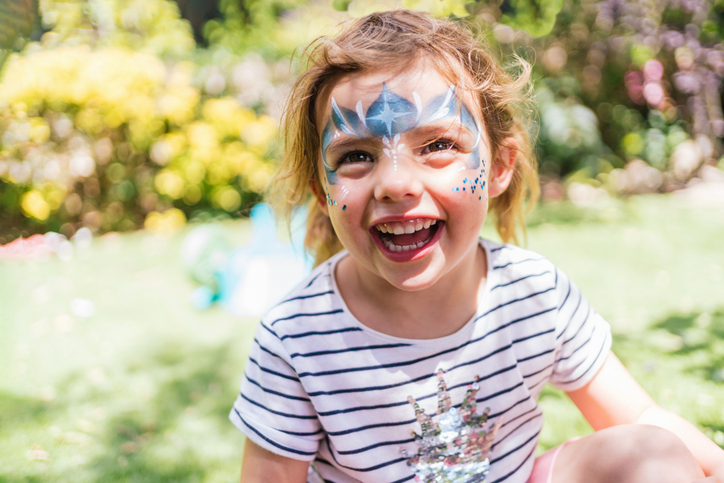 Happy blonde girl with painted face playing outdoors on a sunny day.